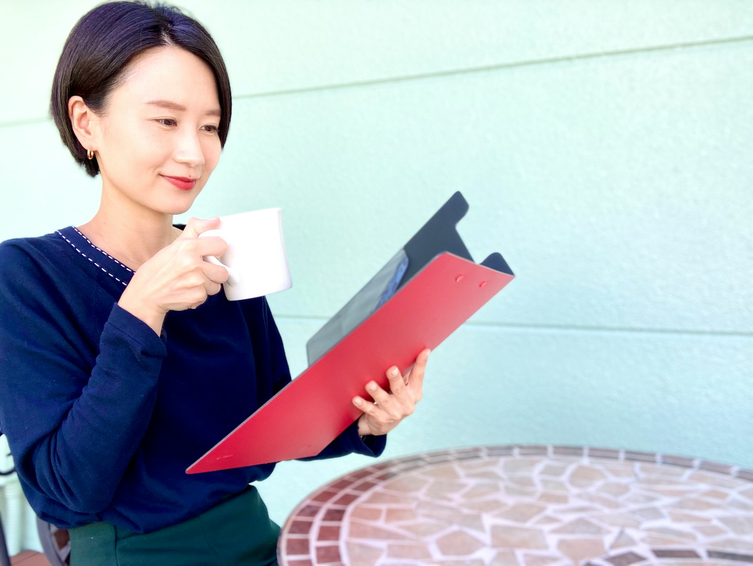 Người phụ nữ ngồi ở bàn cà phê cầm cốc trắng trong khi nhìn vào thực đơn màu đỏ