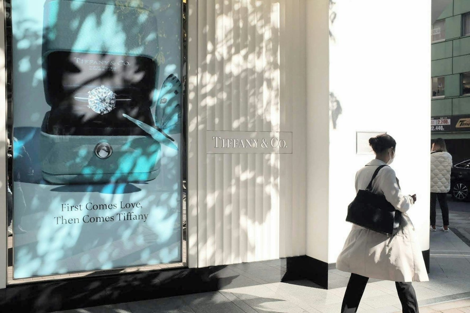 Una vetrina che mostra un orologio su sfondo blu una donna in cappotto bianco che passeggia