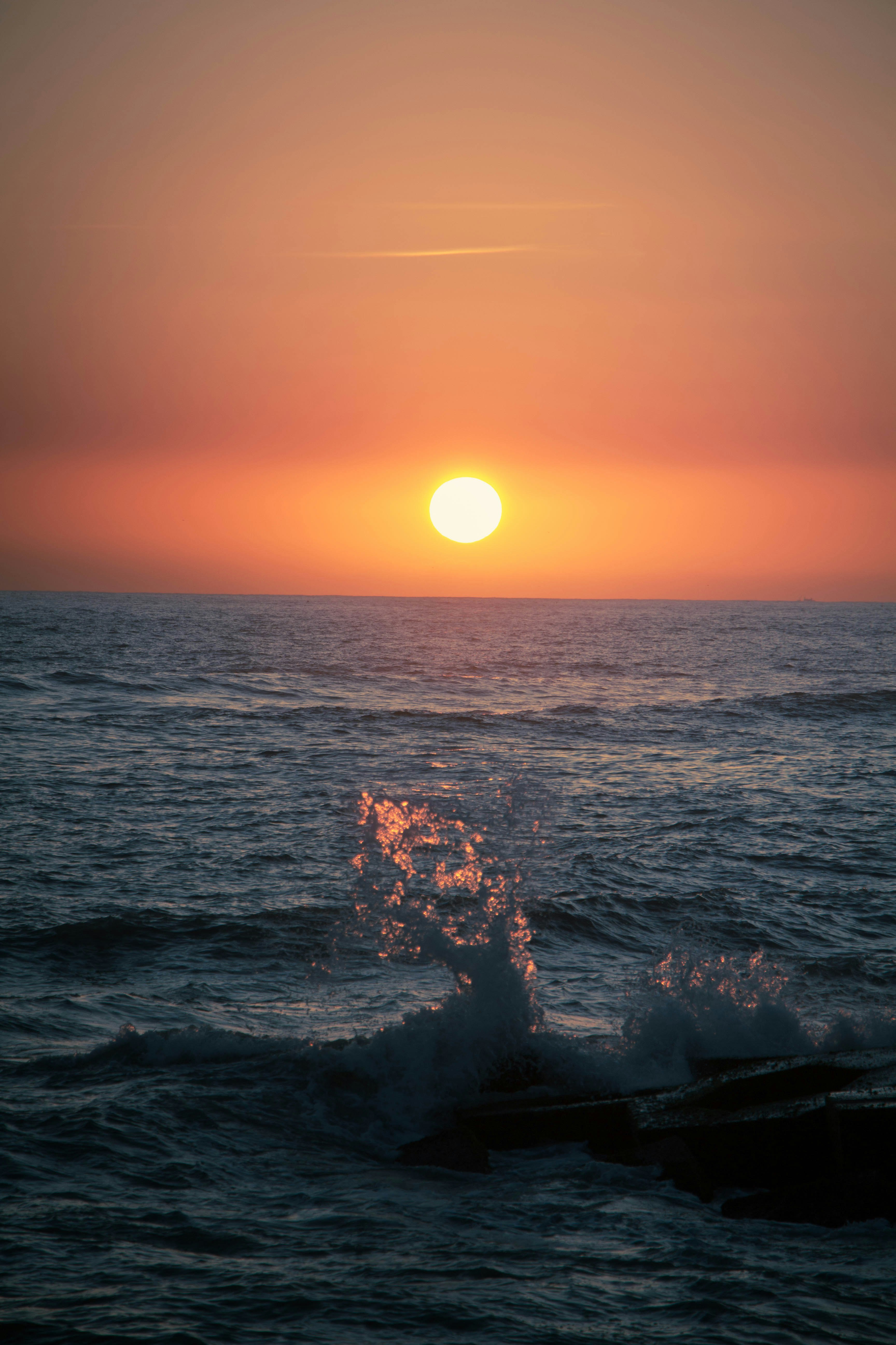 水平線に沈む夕日と波しぶきの海景