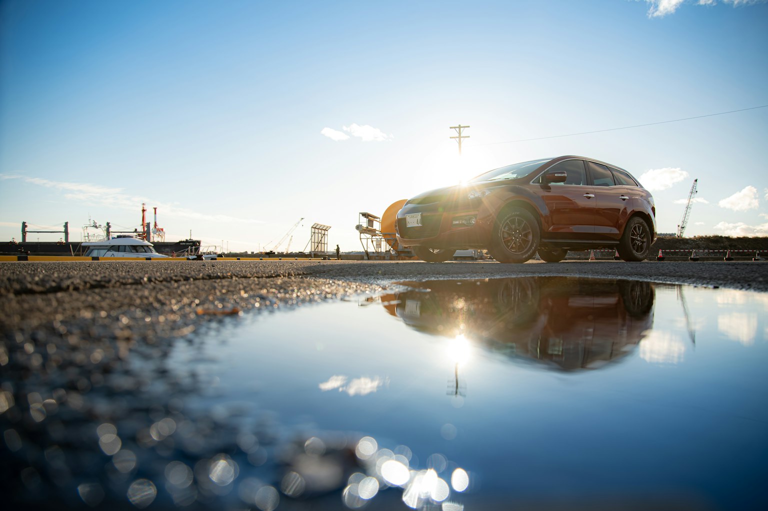 Coche rojo reflejado en un charco con cielo azul