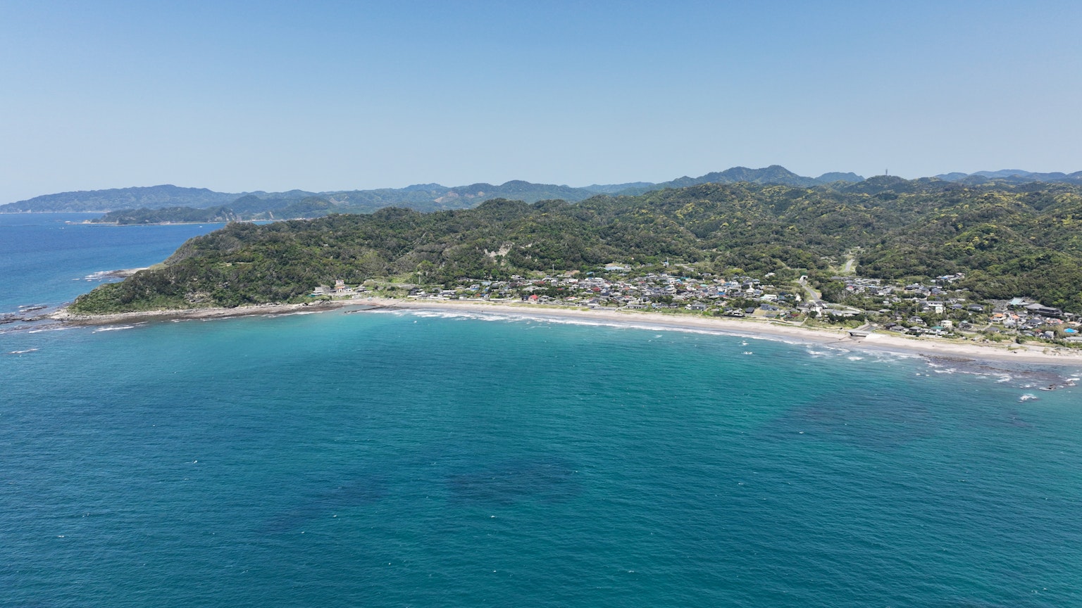 Pemandangan udara pantai yang dikelilingi laut biru dan perbukitan hijau