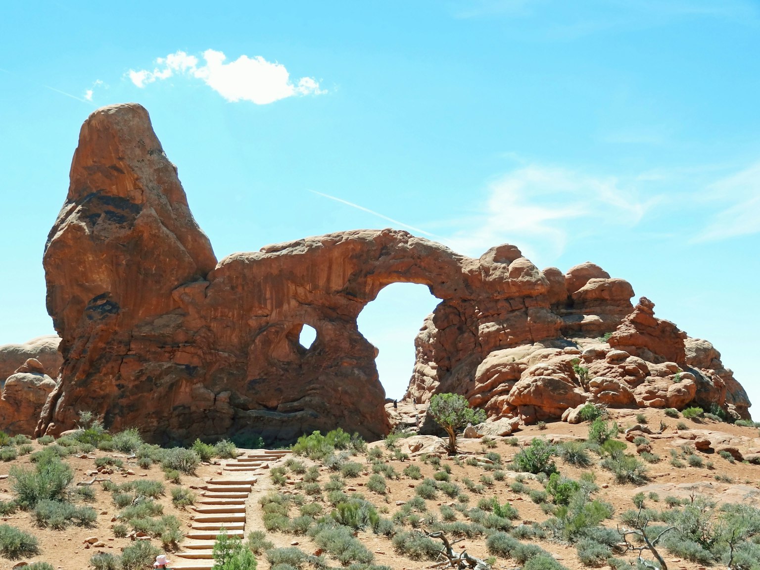 Natural landscape featuring a red rock arch and surrounding shrubs