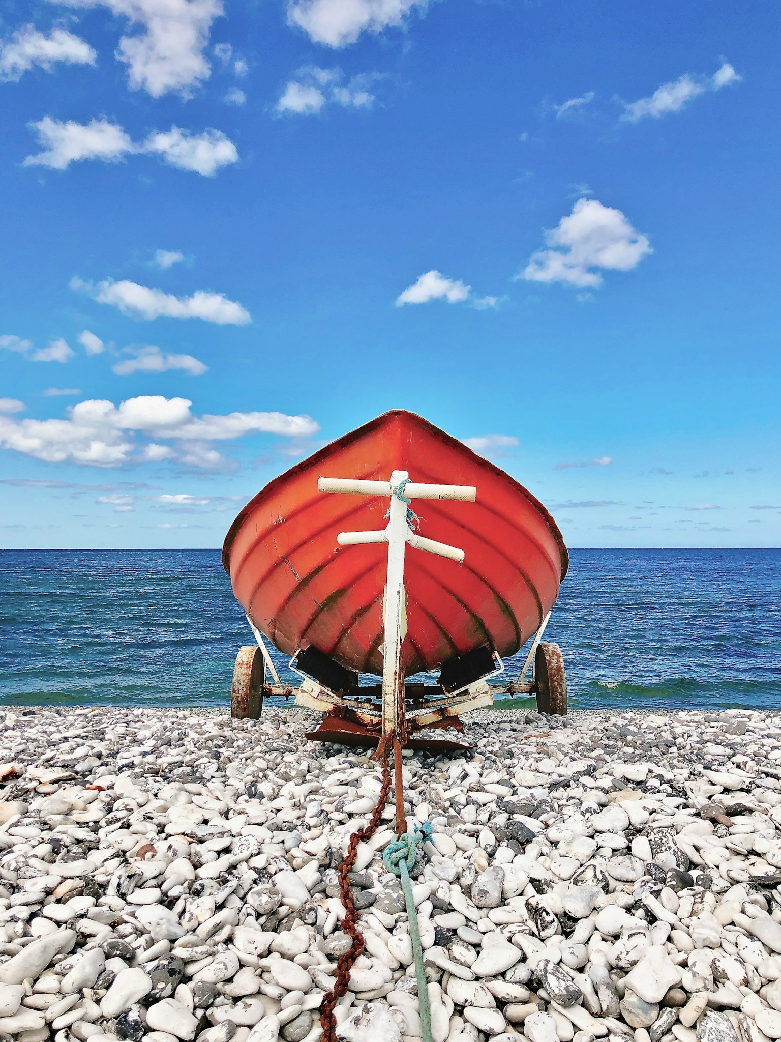 Barco rojo en una playa de guijarros con cielo azul y mar de fondo