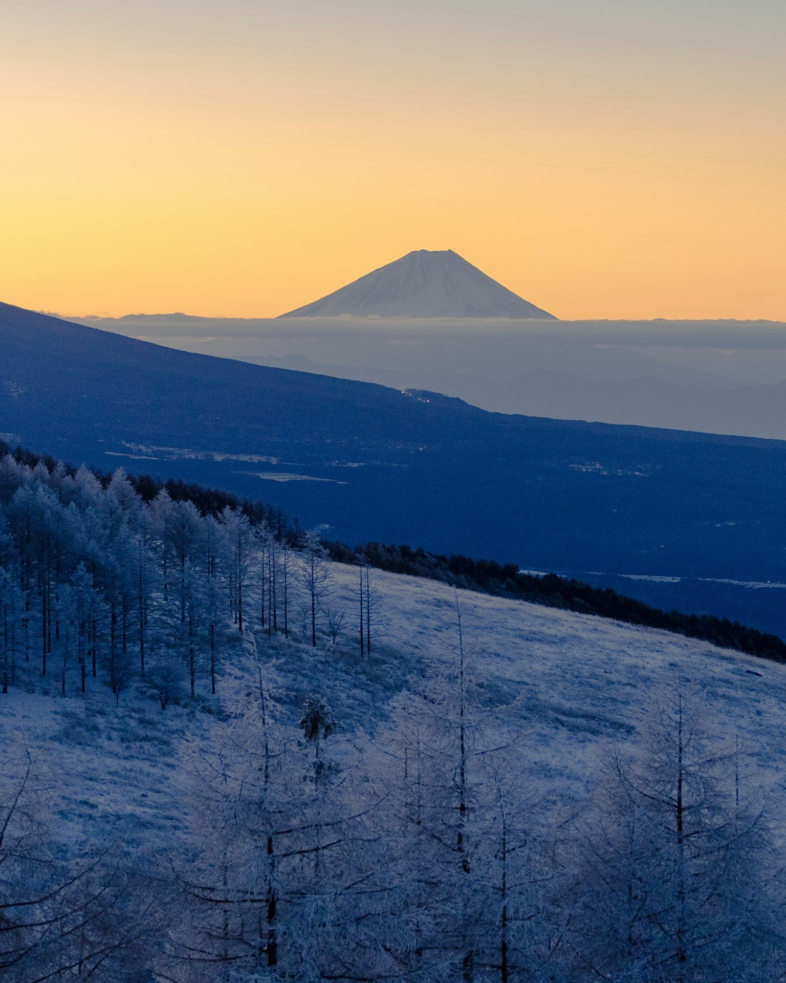 被雪覆蓋的山脈景觀，遠處隱約可見富士山的輪廓