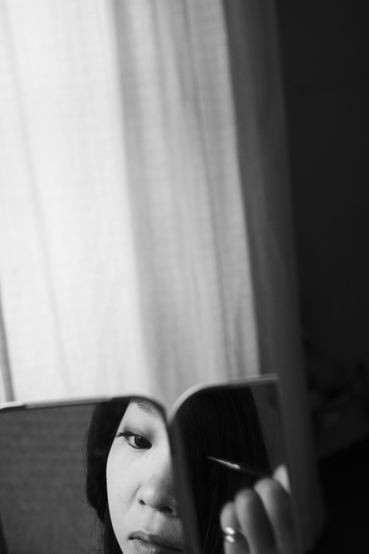 一个女人在镜子前化妆的侧脸，背景有白色窗帘