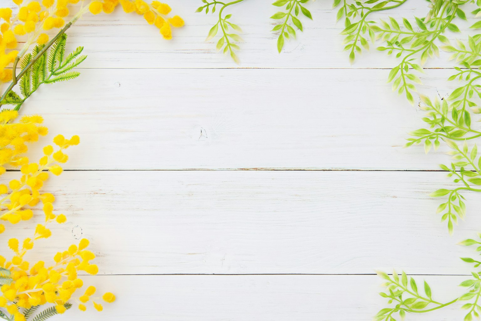 Yellow flowers and green leaves arranged on a white wooden table