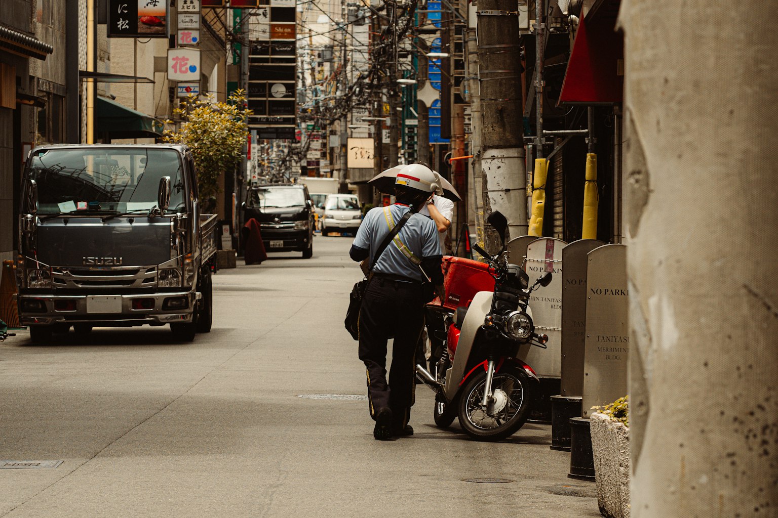 Delivery person standing near a motorcycle in a narrow street holding an umbrella