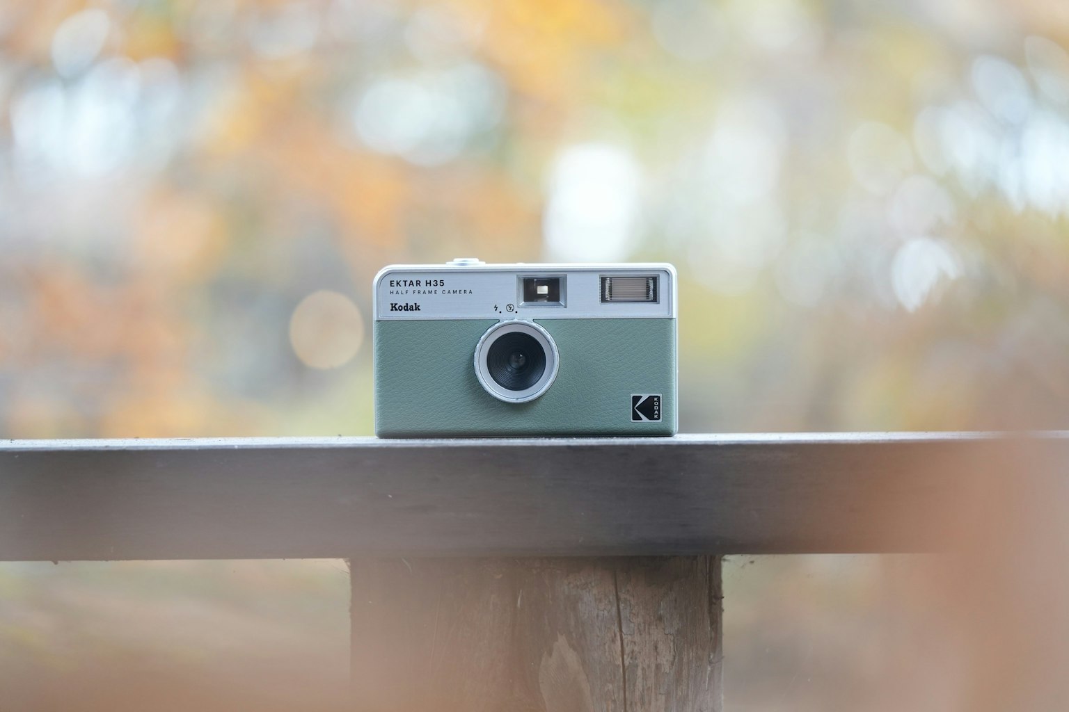 Appareil photo vert posé sur une table en bois avec un arrière-plan flou d'automne
