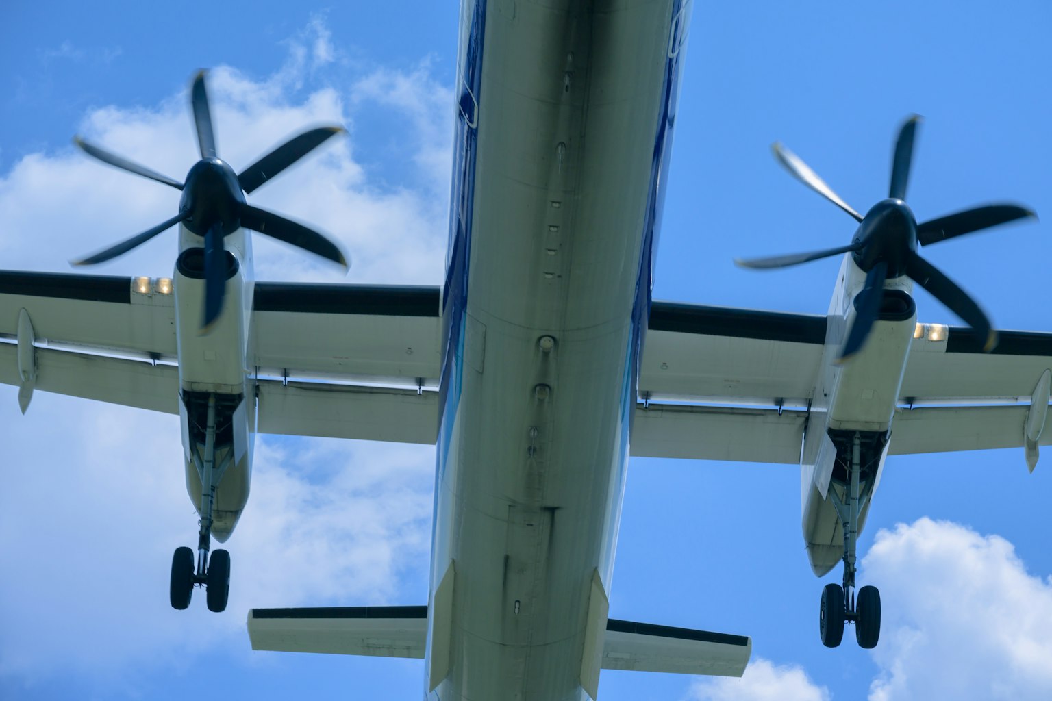 Unteransicht eines Propellerflugzeugs mit blauem Himmel und weißen Wolken