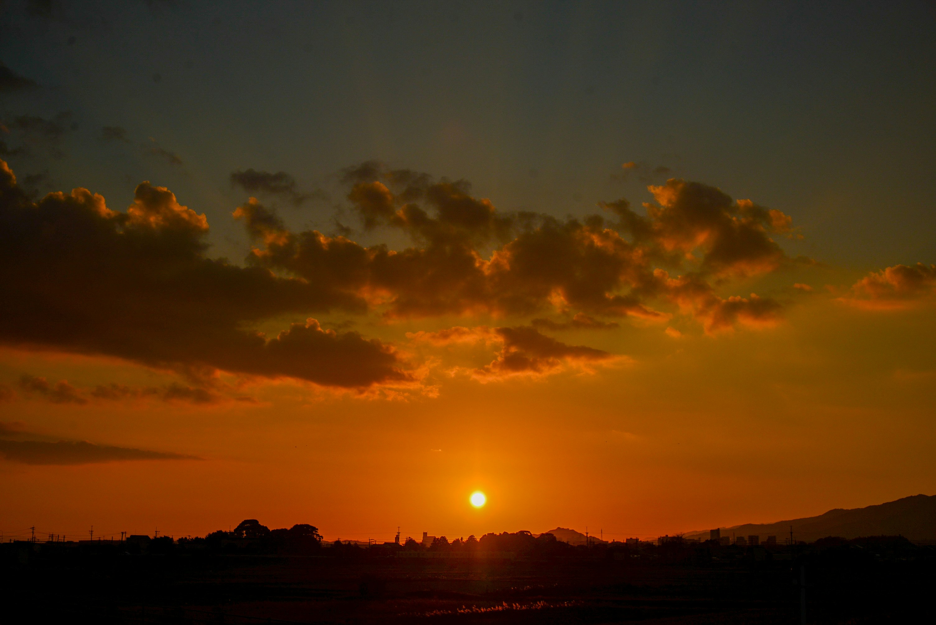 夕暮れの空に広がるオレンジ色の雲と沈む太陽の光