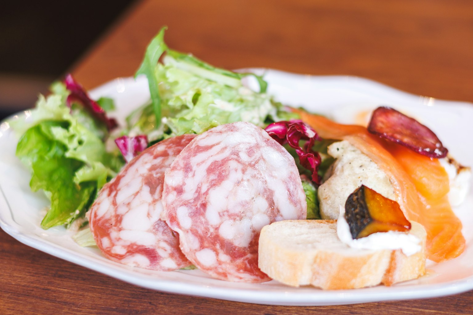 Plate featuring salami and smoked salmon accompanied by fresh salad and baguette