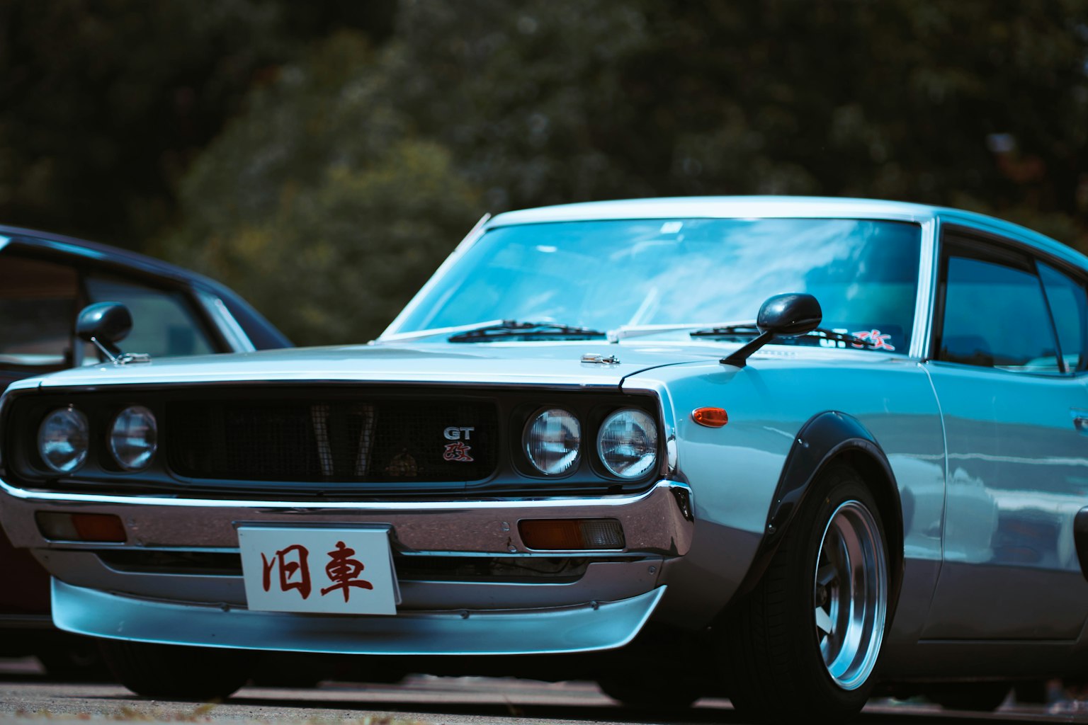 Classic silver Japanese car in the foreground with trees in the background