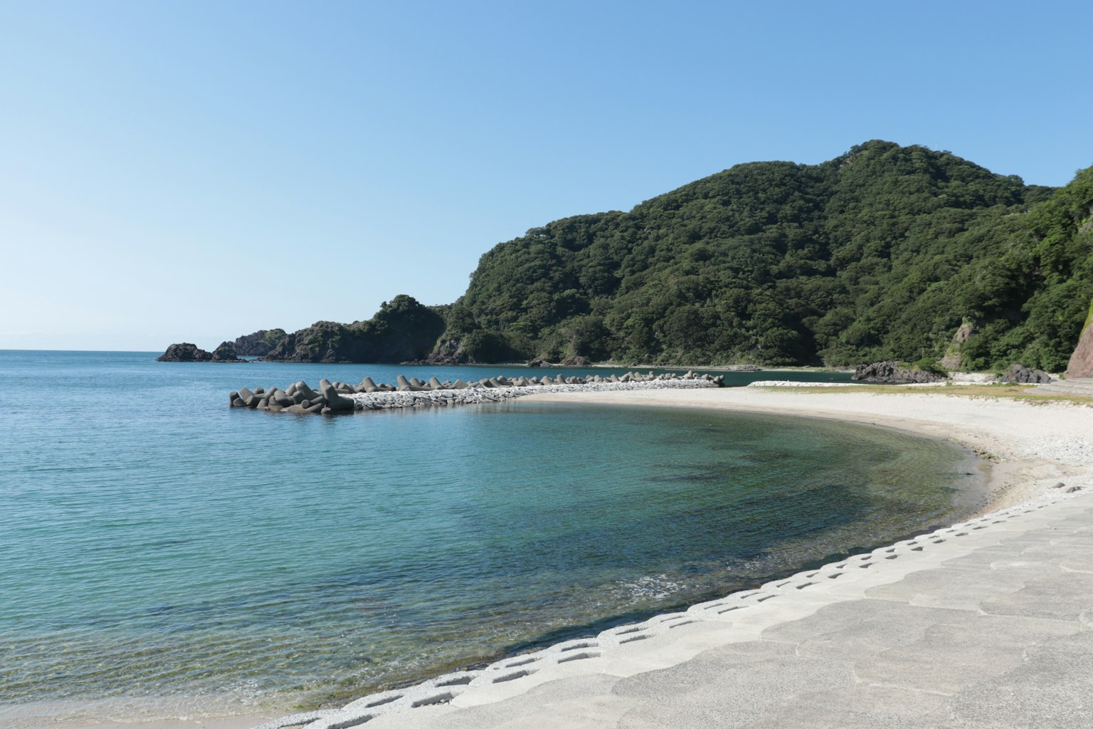 Pemandangan pantai tenang dengan laut biru dan pegunungan hijau
