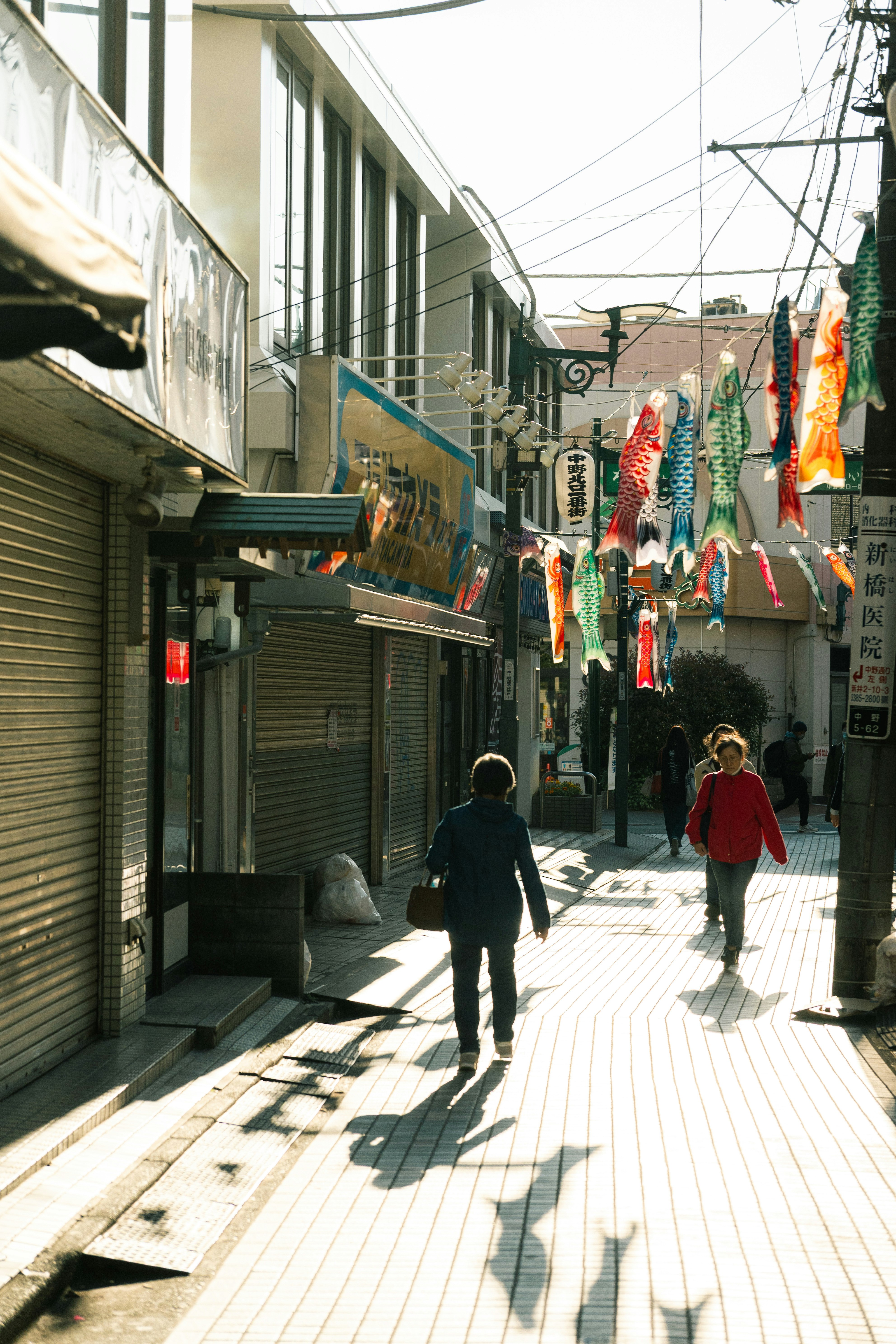 路地の軒先に並ぶ鯉のぼりと人のいる商店街