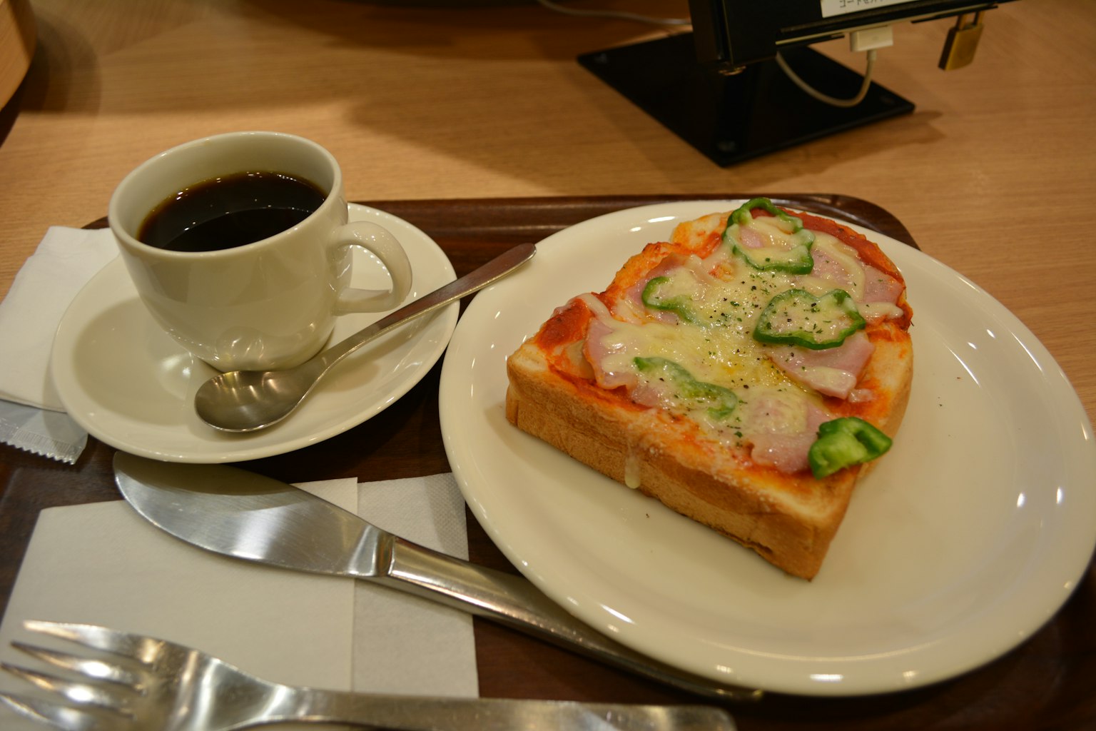 Plato con tostada cubierta de jamón y verduras junto a una taza de café