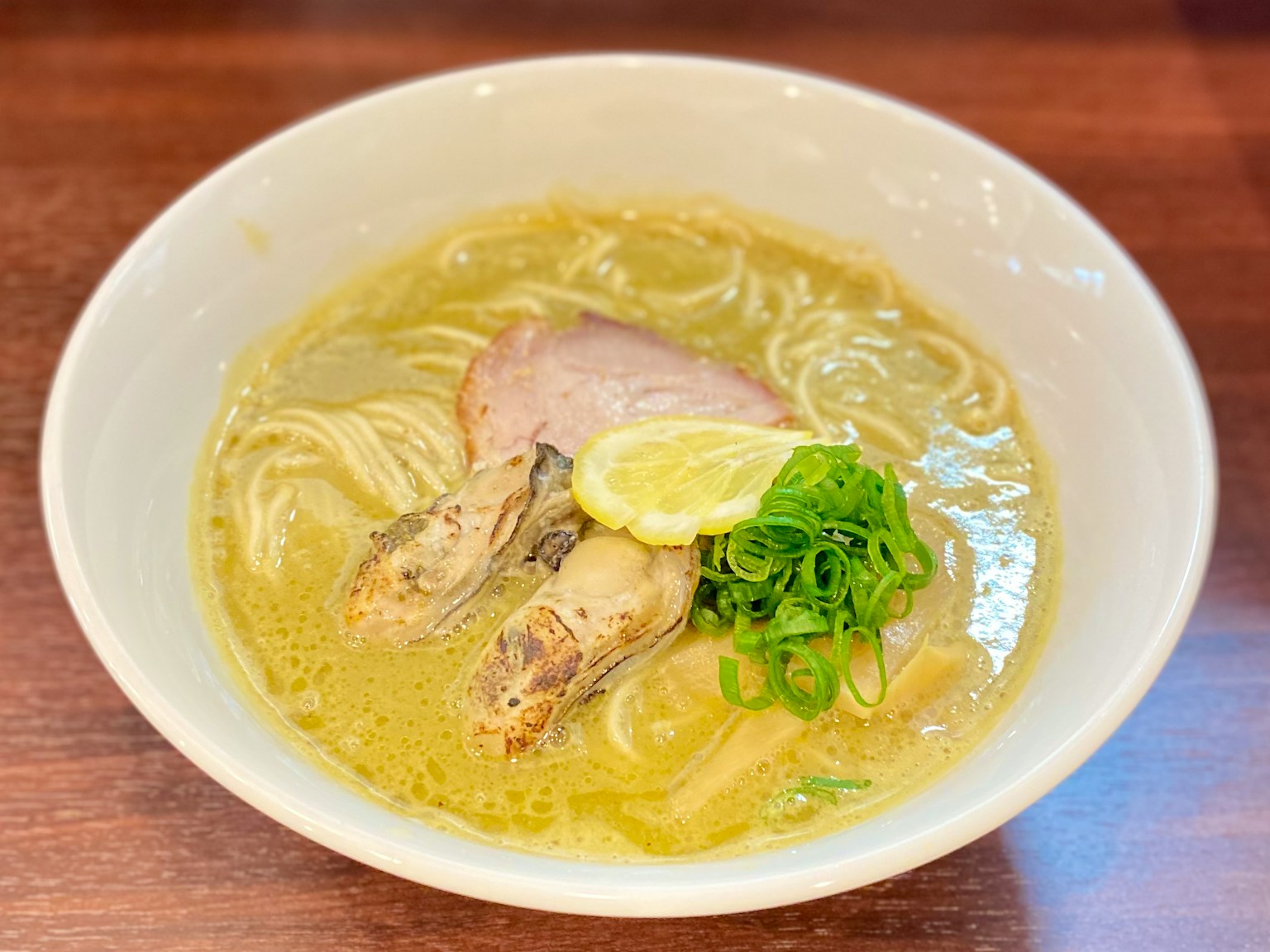 Bowl of ramen featuring sliced pork, green onions, lemon, and noodles