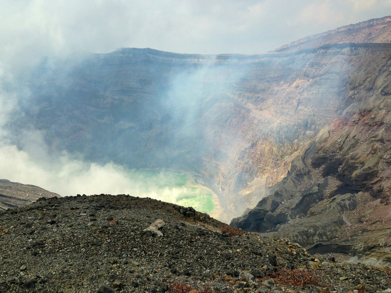 Volcanic crater with green lava and smoke in the background