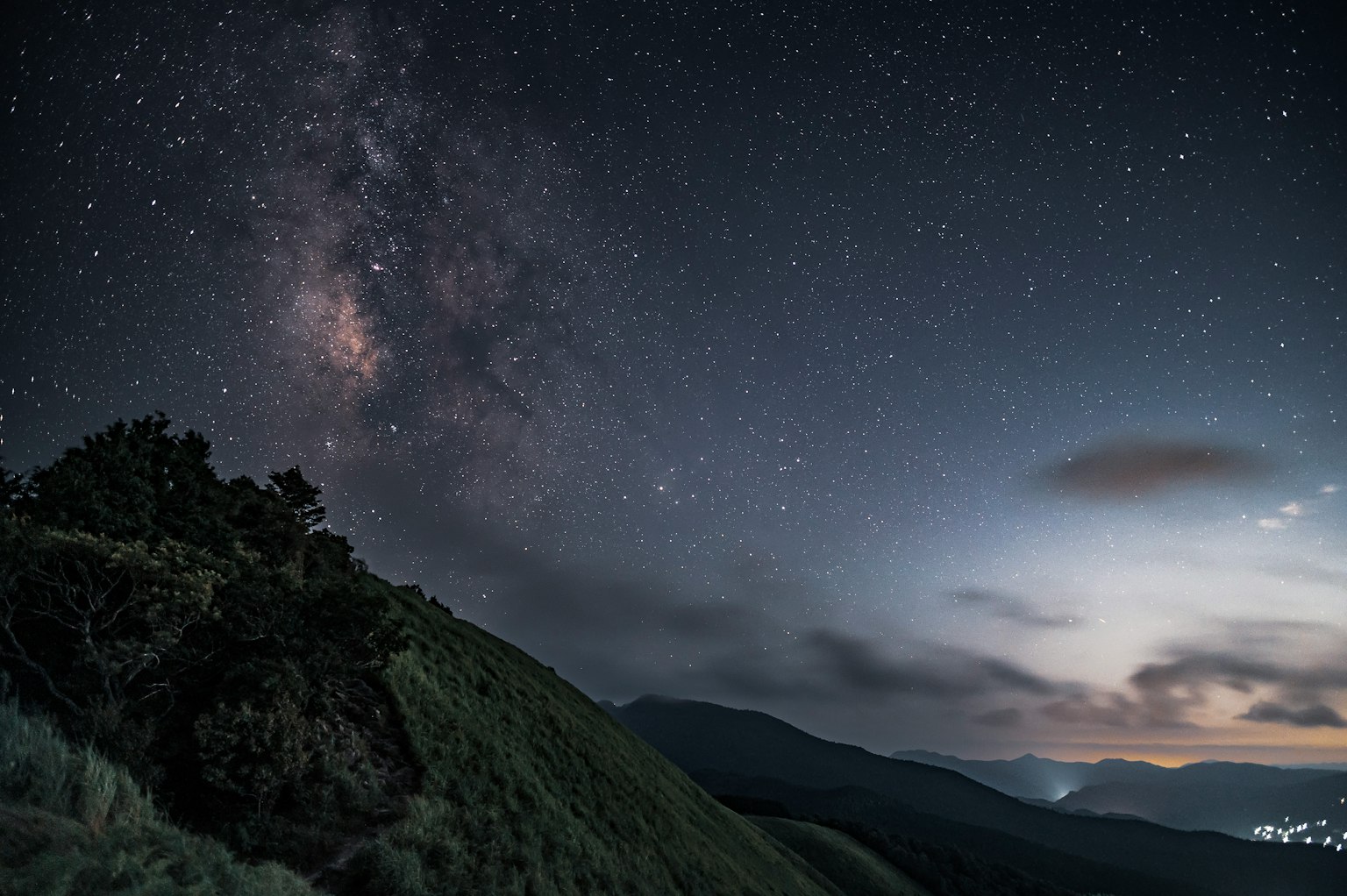 夜間景觀，星空和銀河在綠色山丘和山脈上可見