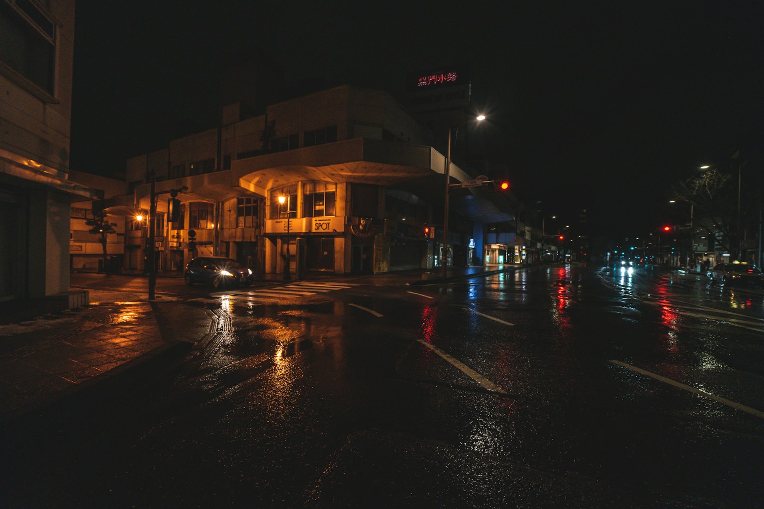 Ruhige Straßenecke bei Nacht mit nassen Straßen und orangefarbenen Straßenlaternen