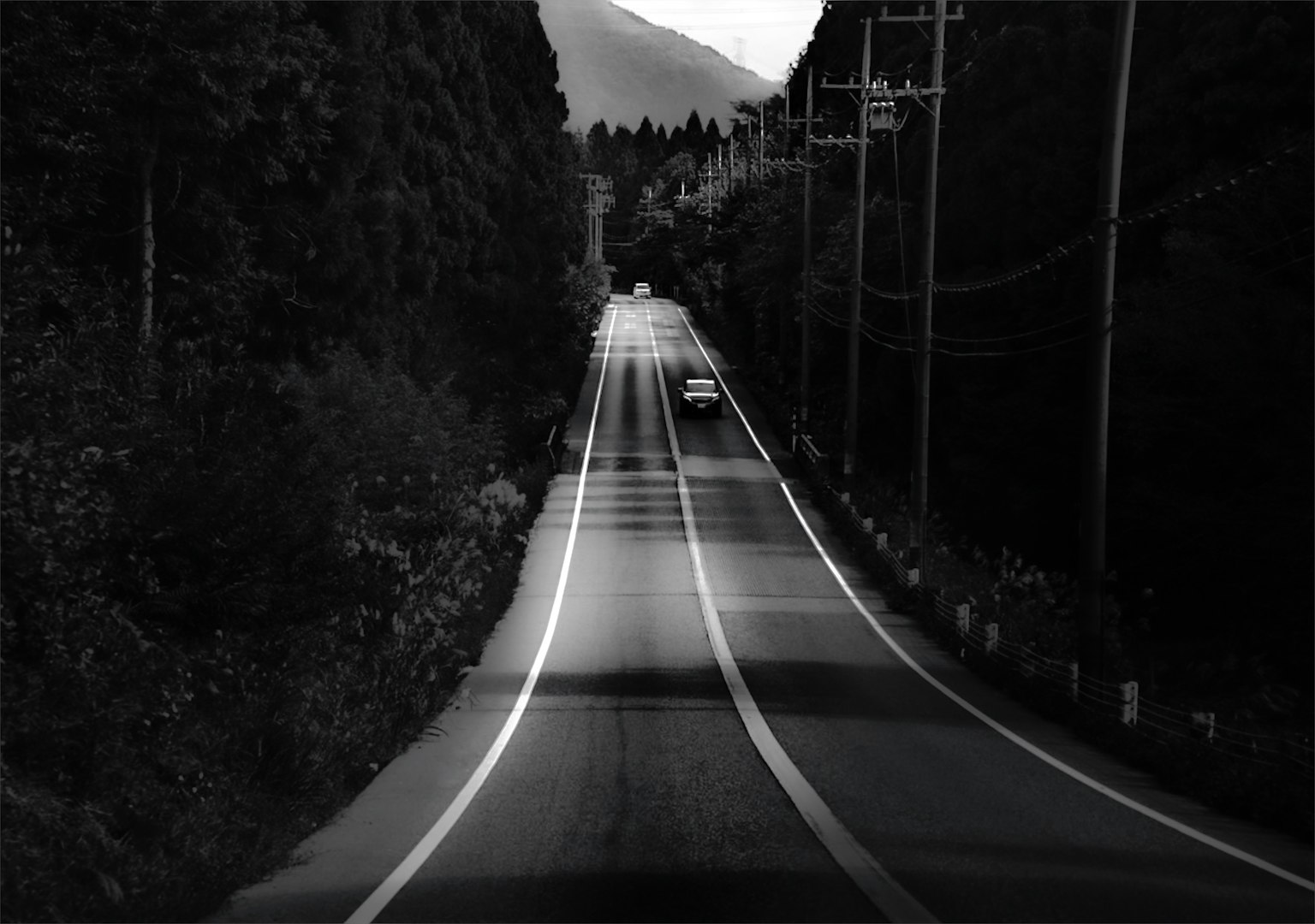 Black and white landscape of a road surrounded by mountains and trees