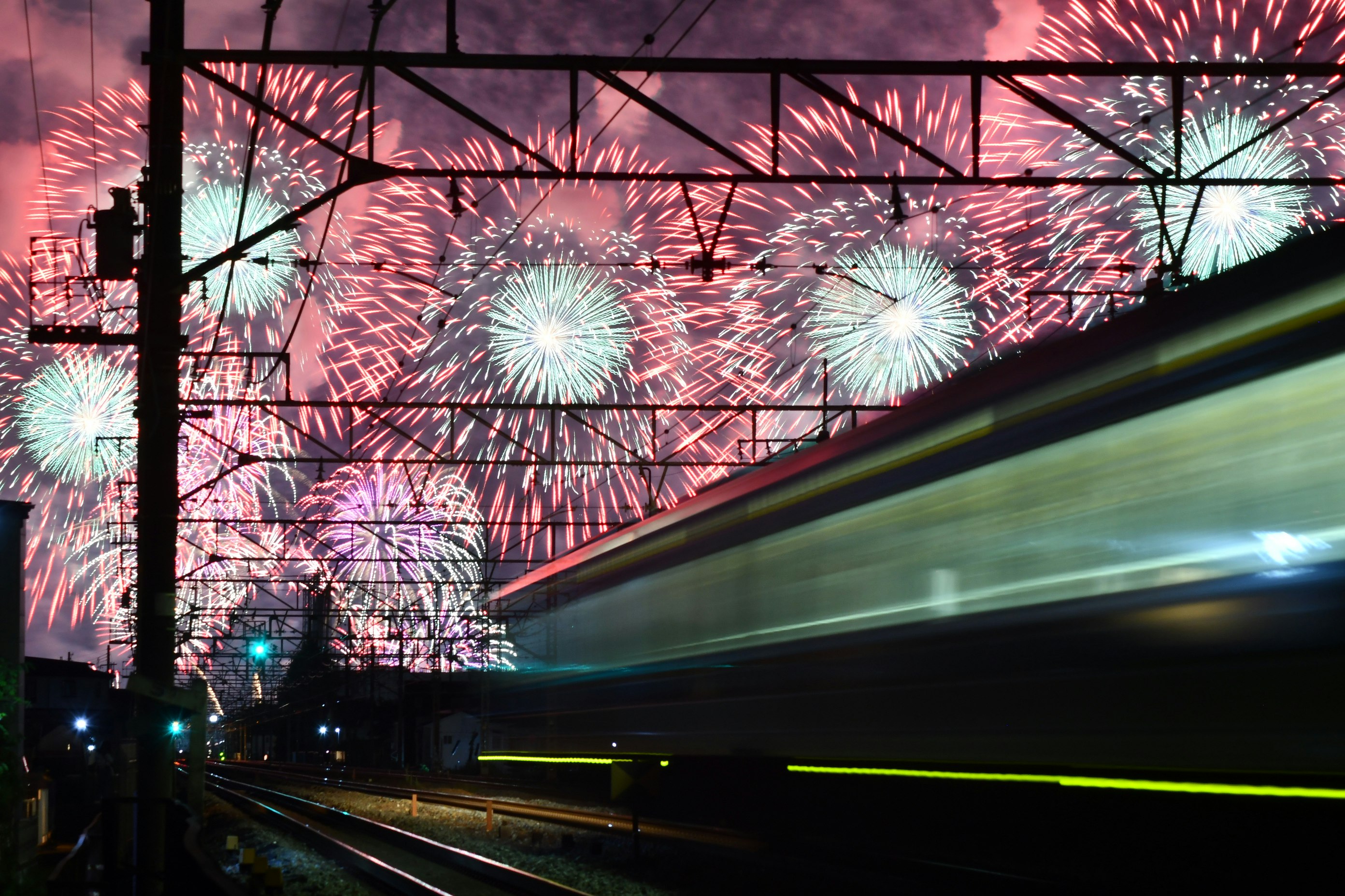 線路上を走る電車と夜空に広がる花火