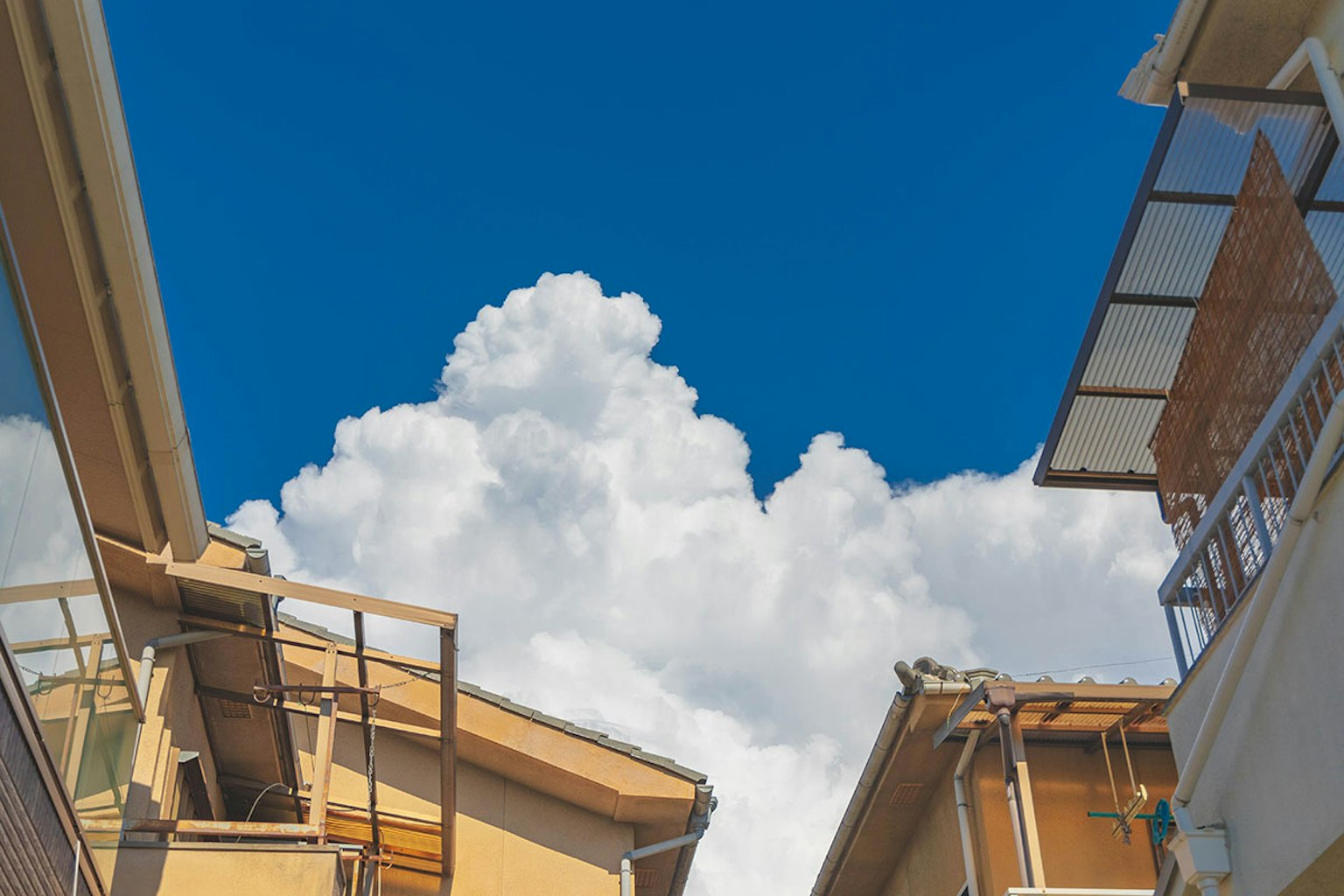 Une vue entre des bâtiments sous un ciel bleu avec des nuages blancs duveteux