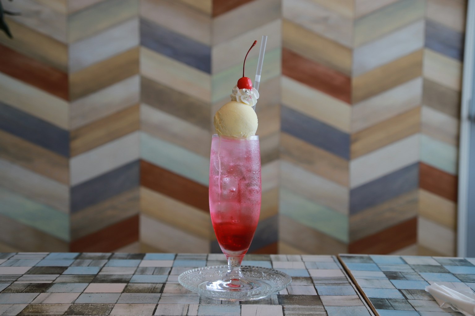 Una bebida rosa decorada con helado y una cereza frente a un fondo de chevron colorido