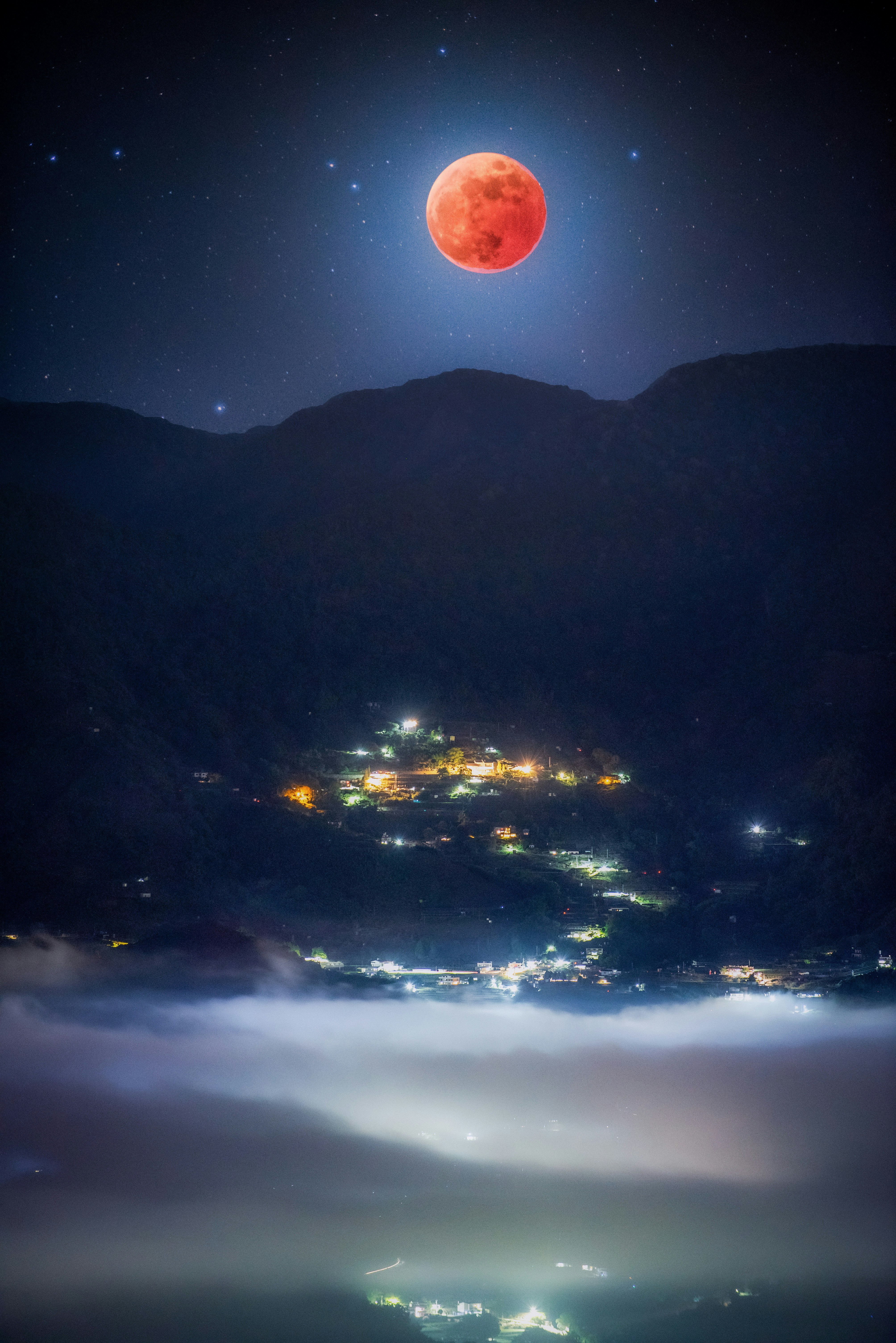 夜空に浮かぶ赤い満月と山あいの街明かり