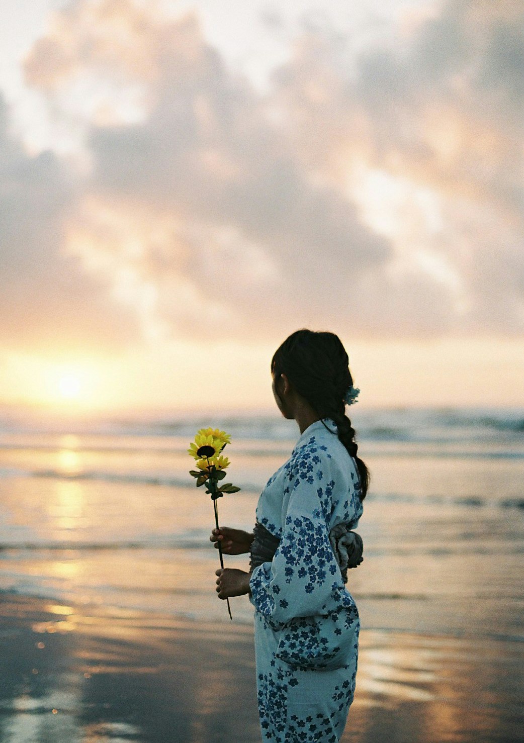 夕暮れの海辺でひまわりを持つ女性