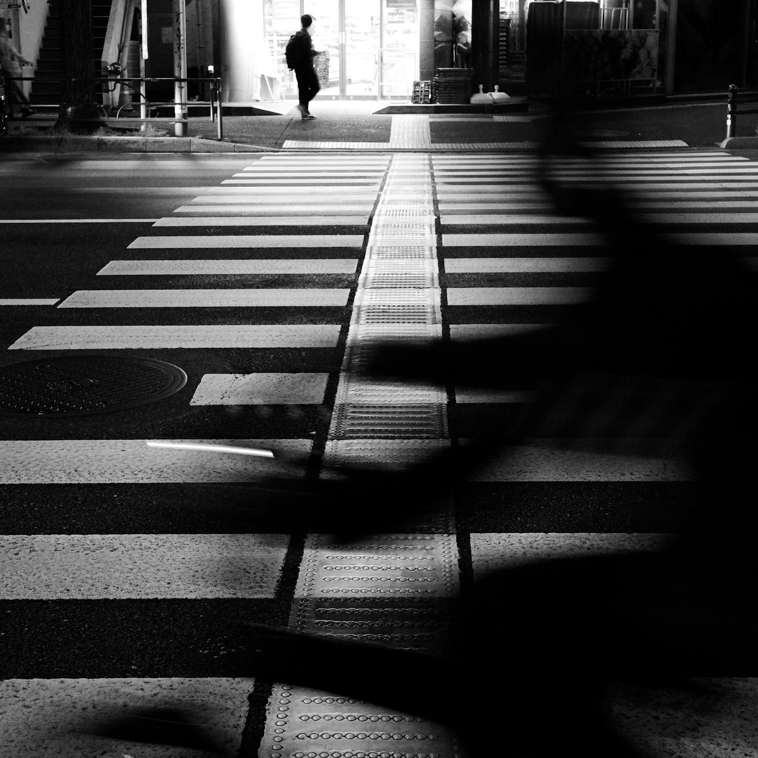 Silhouette di un pedone e di un ciclista che attraversano una striscia pedonale in bianco e nero
