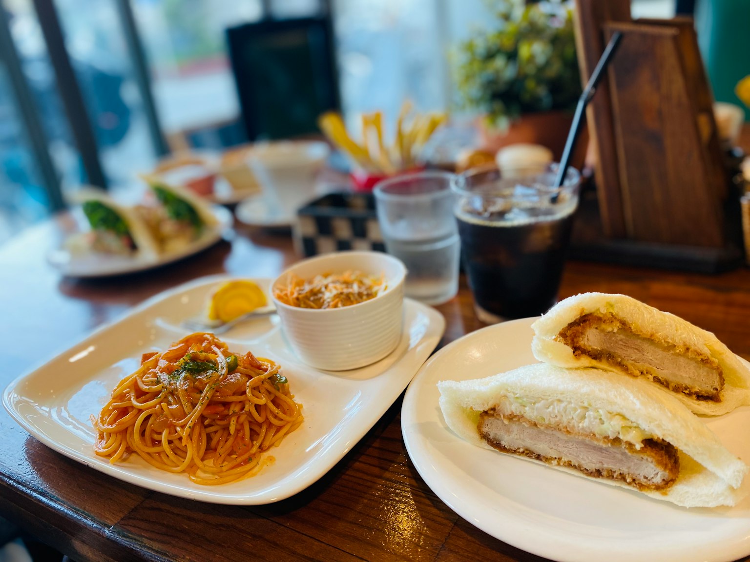 A table set with a meal featuring pasta, soup, and a katsu sandwich