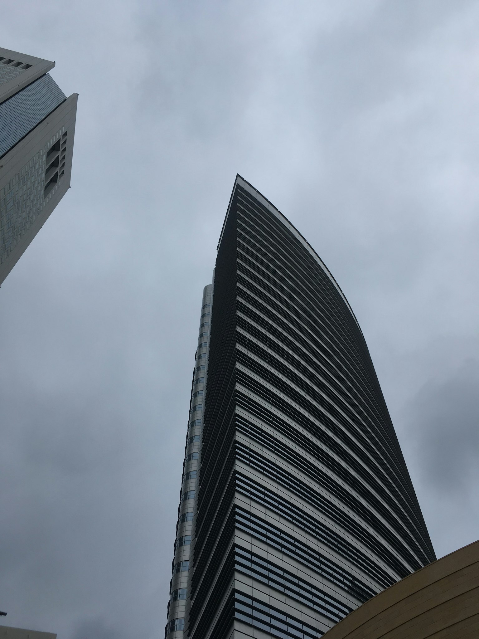 從下方仰望現代摩天大樓，背景為陰雲密布的天空