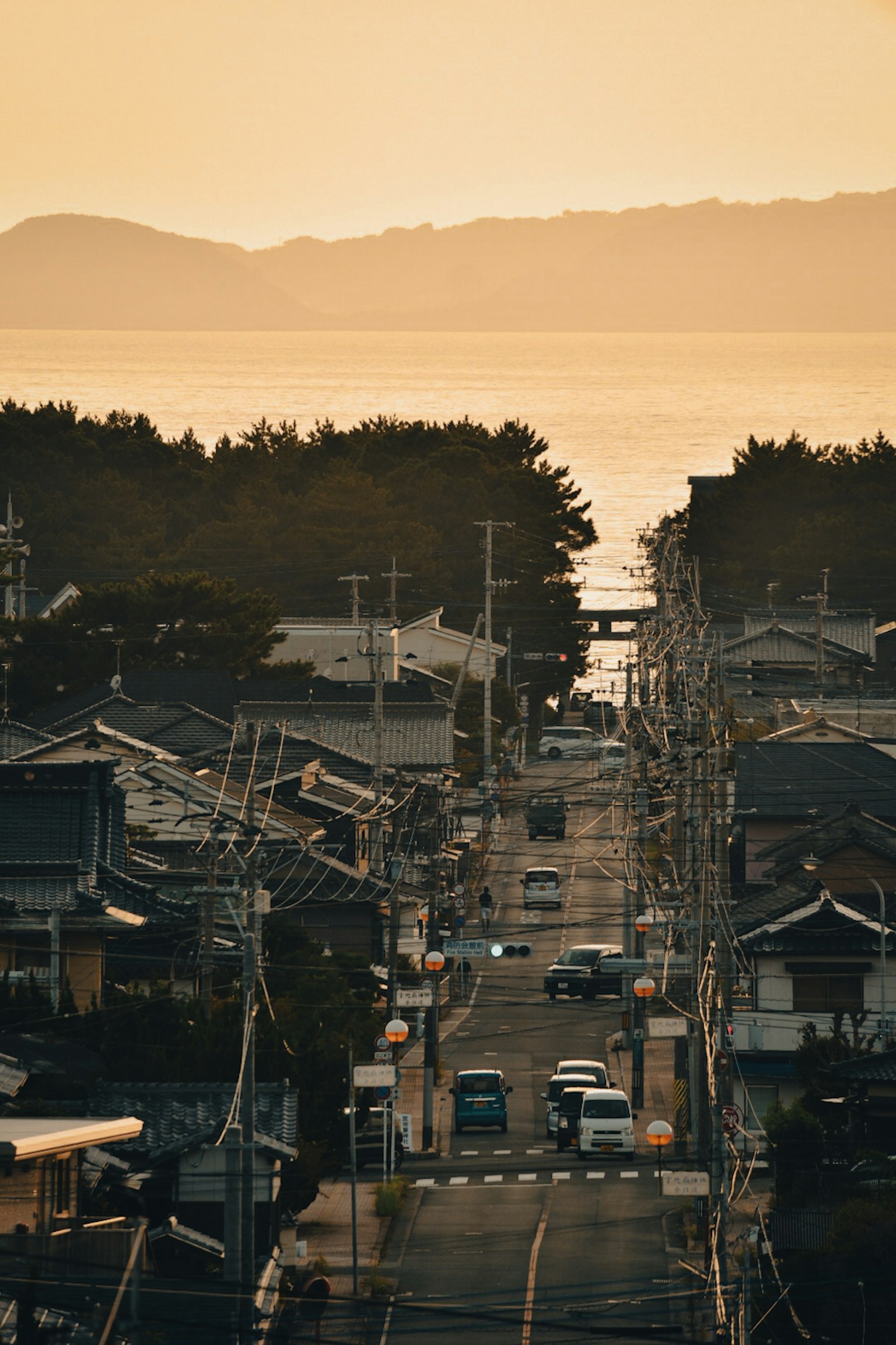 黄昏时分的海滨小镇 道路旁的房屋和车辆 温暖的橙色天空