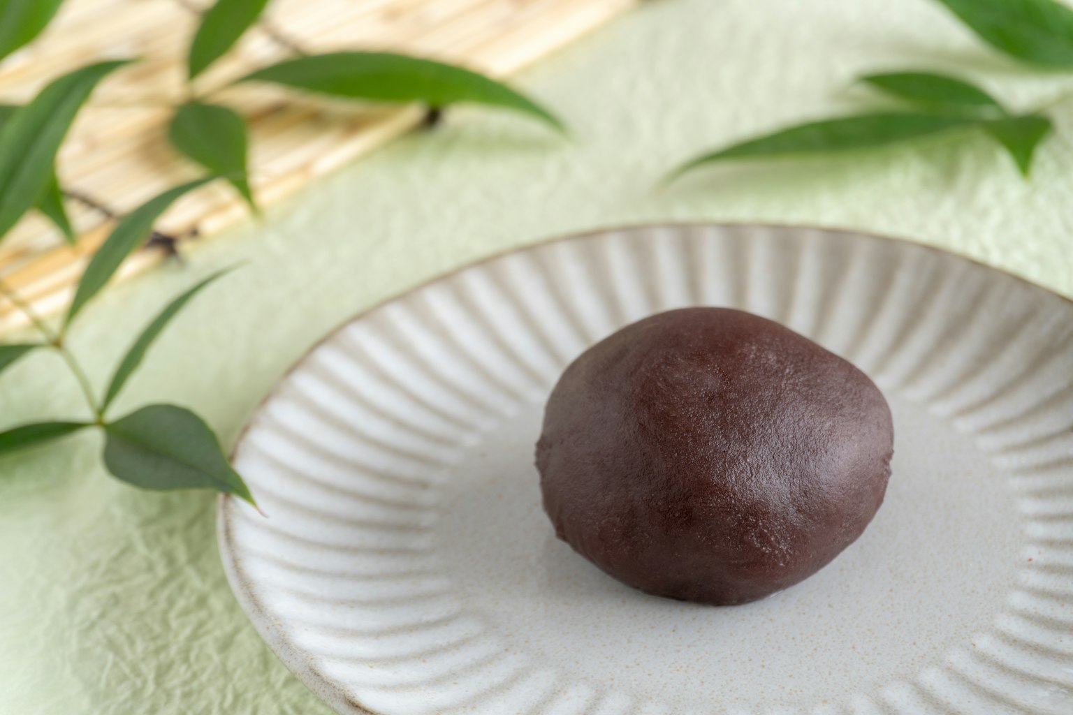 A shiny black Japanese sweet on a white plate against a green background