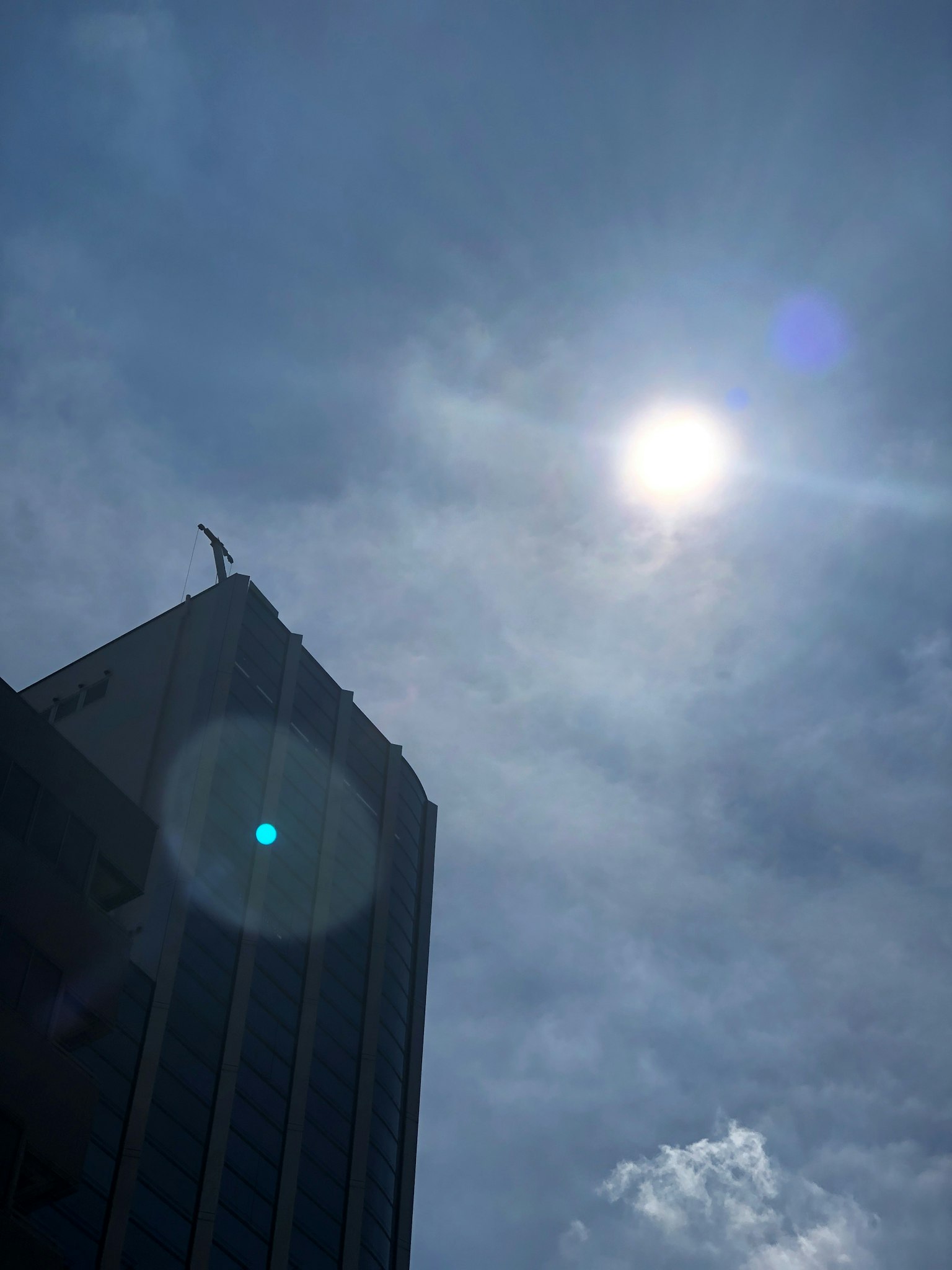 Edificio alto con una statua in cima e sole luminoso contro un cielo nuvoloso