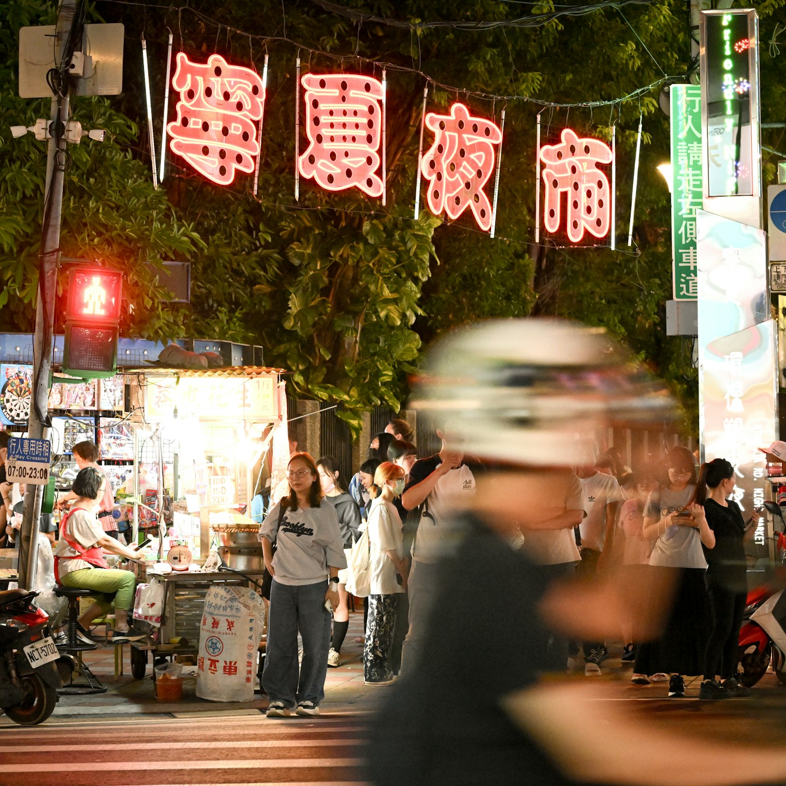 Scène animée de marché nocturne avec des gens rassemblés et des stands de nourriture illuminés