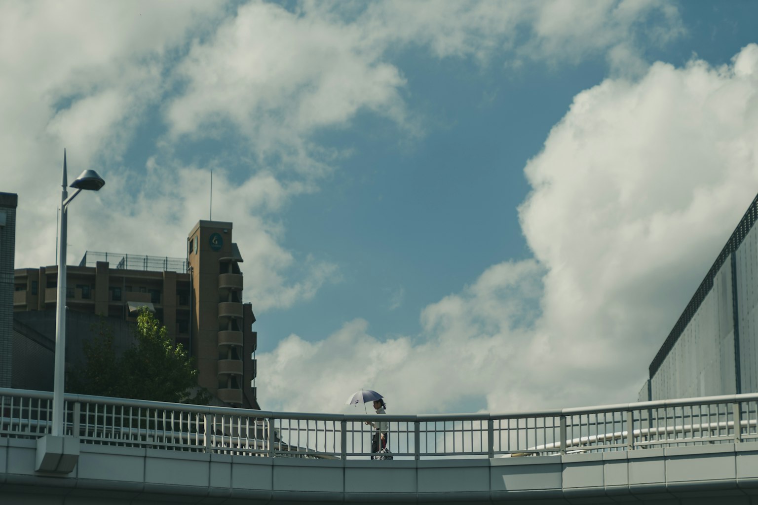 Person geht über eine Fußgängerbrücke unter blauem Himmel mit Wolken