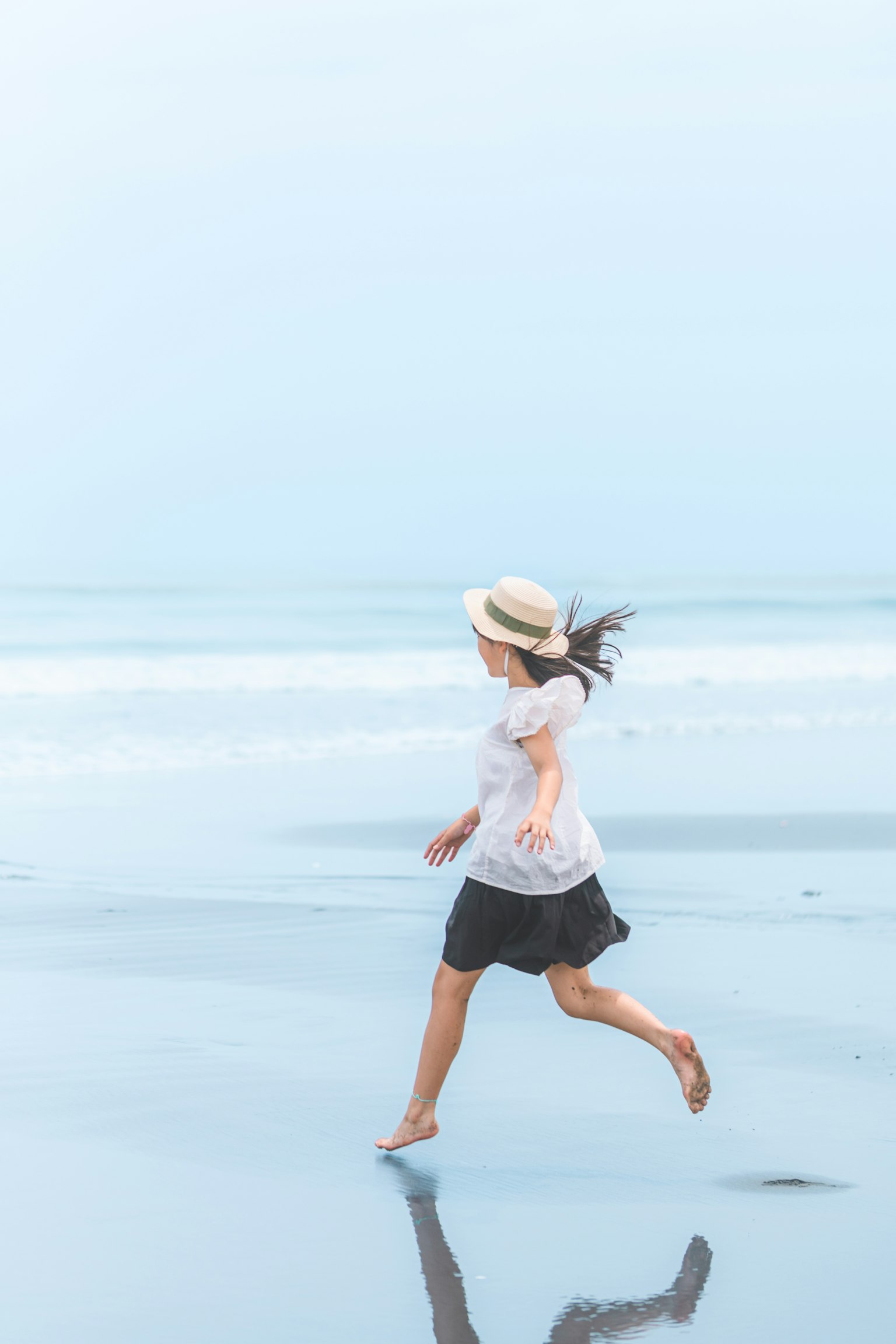 Girl running on the beach wearing a white shirt and black skirt with a hat