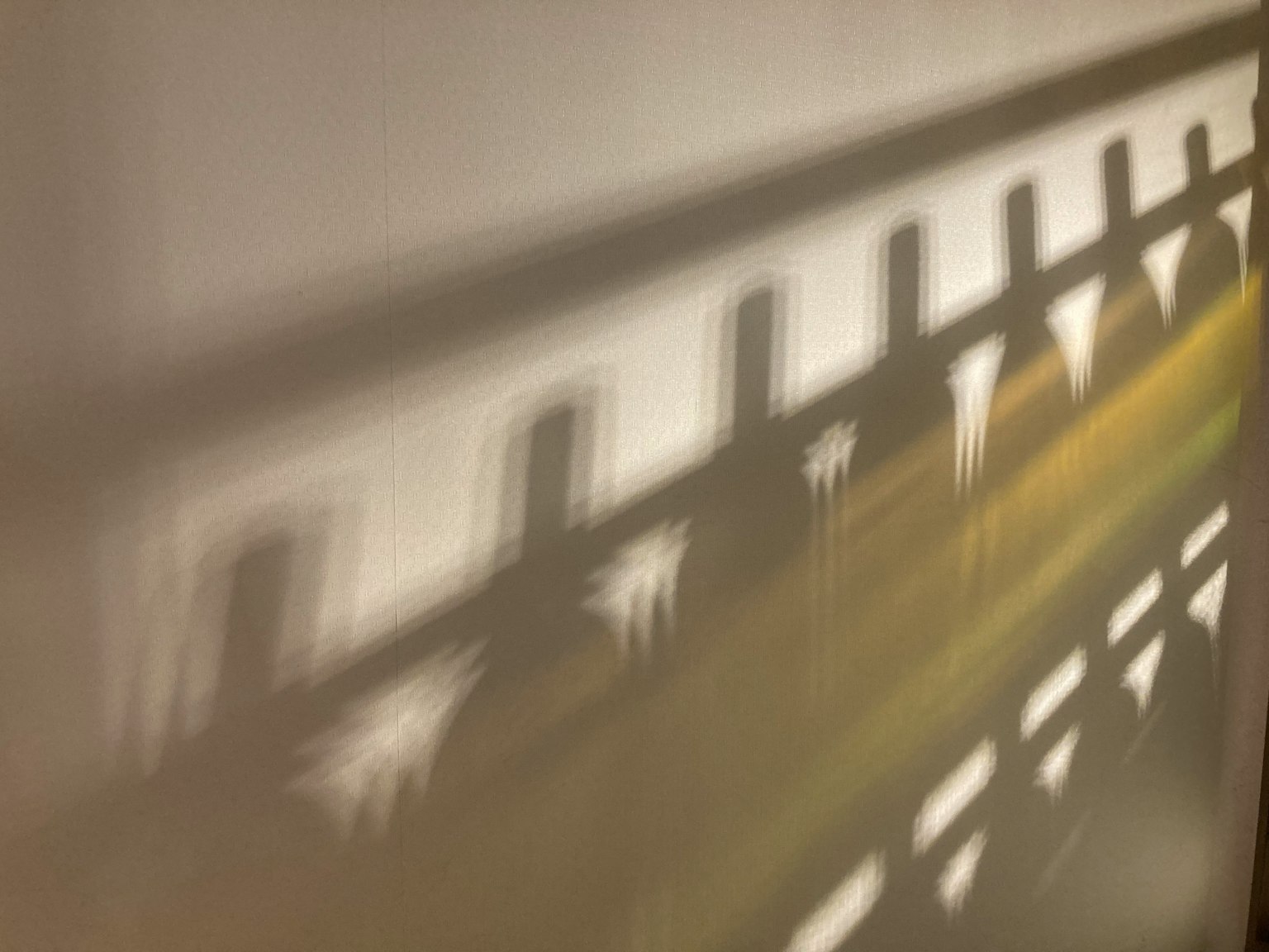 Shadows of a fence cast on a wall with light creating patterns