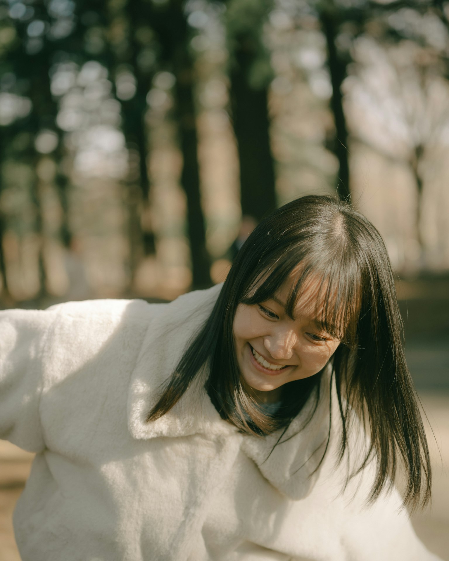 Woman smiling in a park wearing a white coat surrounded by trees