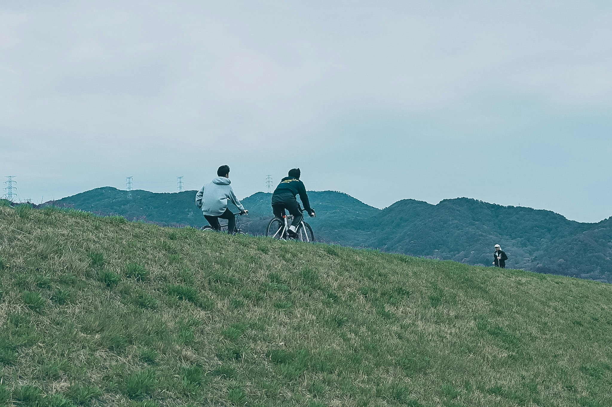 草原の丘を歩く人と自転車のある風景