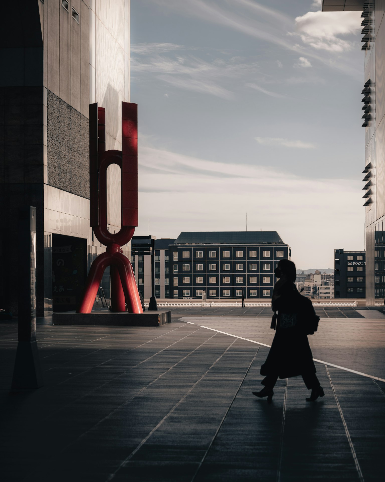 Silhouette of a person walking in front of a red sculpture in a modern urban landscape