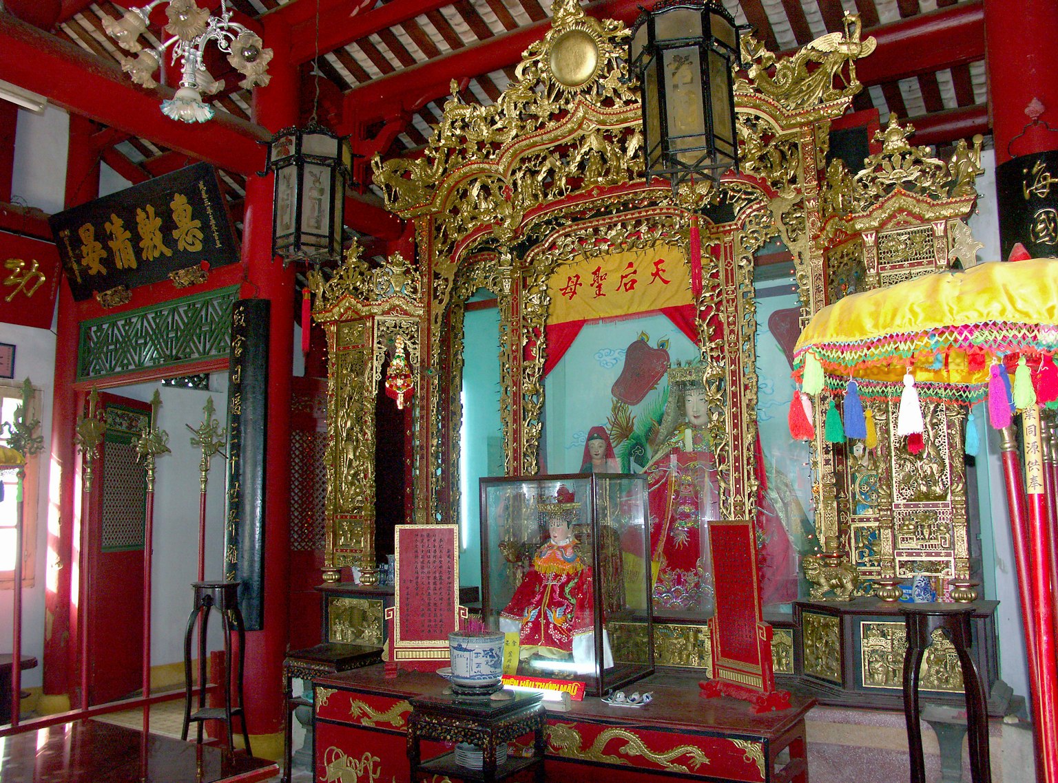 Interior of a temple featuring red and gold decorations with an altar and a statue showcasing traditional Chinese cultural elements