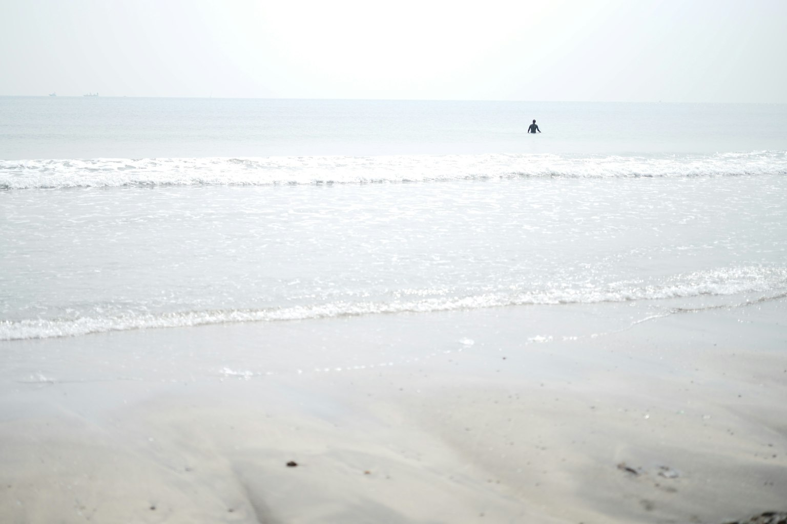 A solitary figure standing at a calm shoreline with gentle waves