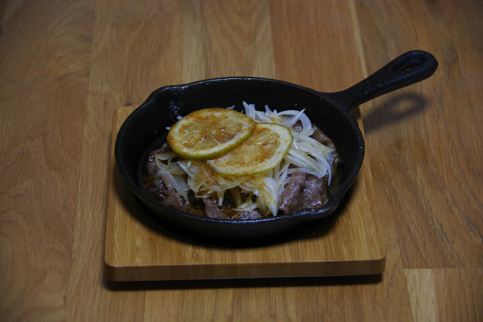 Un piatto in padella con carne e cipolle guarnito con fette di limone