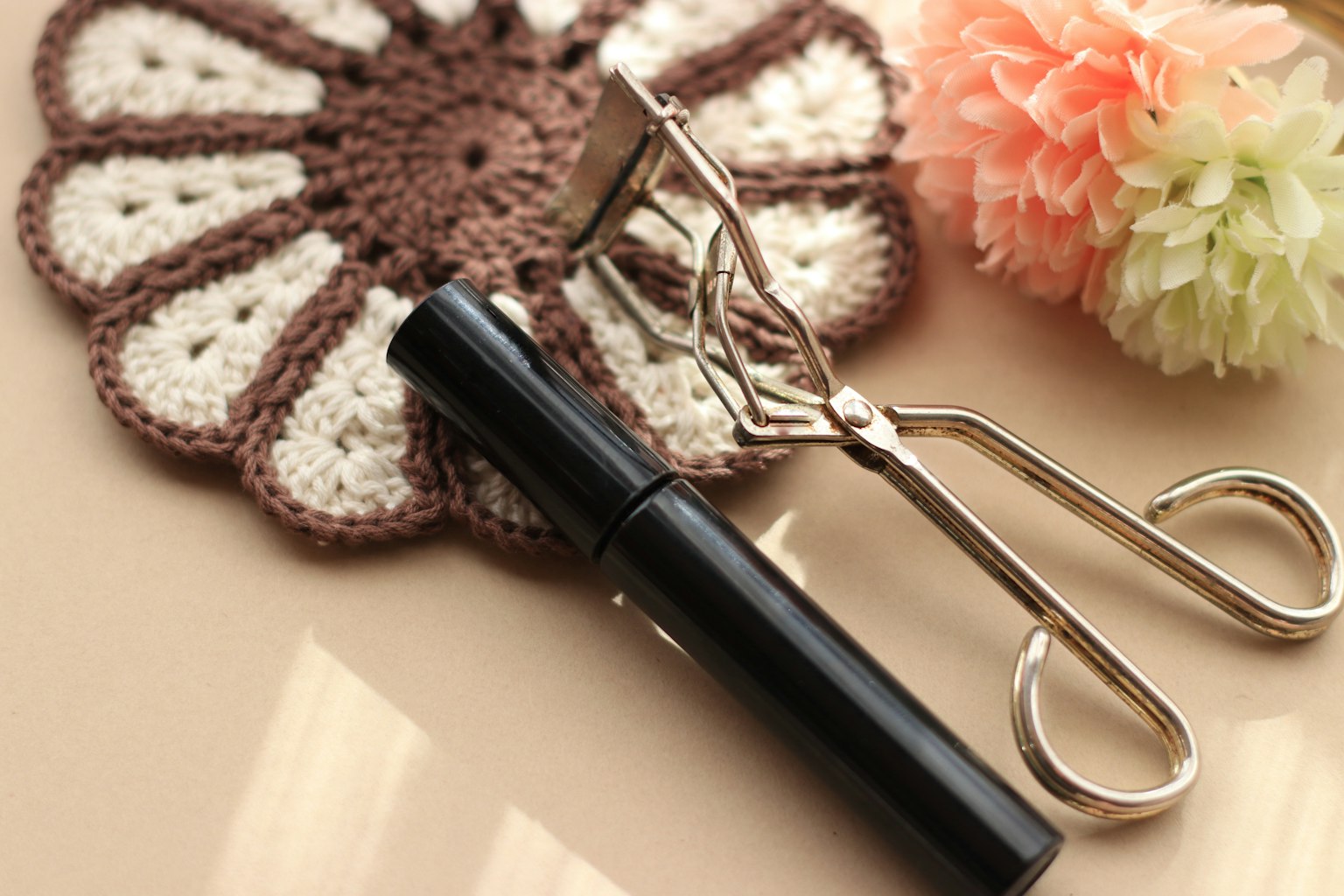 Mascara noir et recourbe-cils posés sur une nappe en dentelle