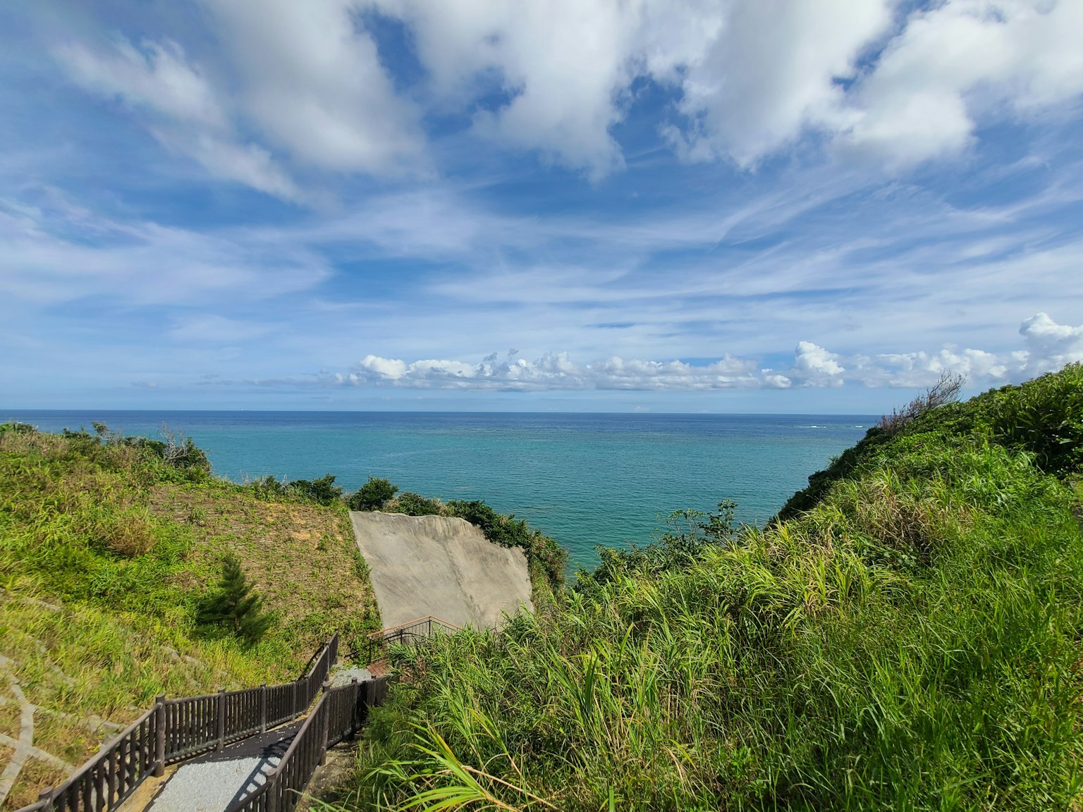 Vista panoramica dell'oceano blu e del cielo con colline verdi e una scala