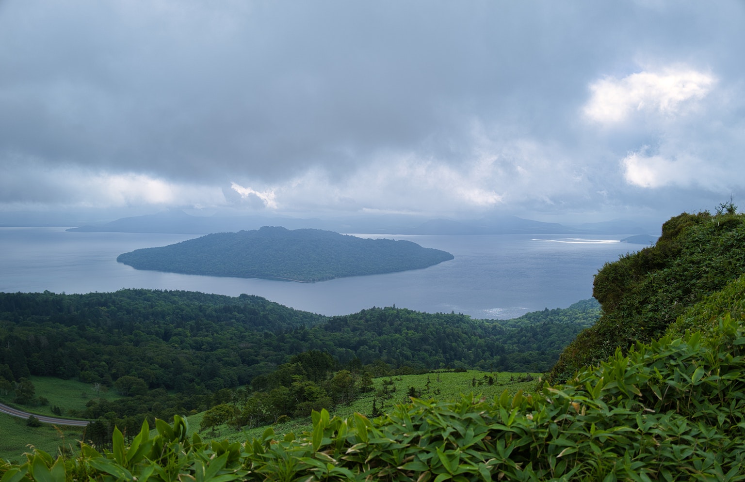 View from a mountain showing lush greenery and an island under a cloudy sky