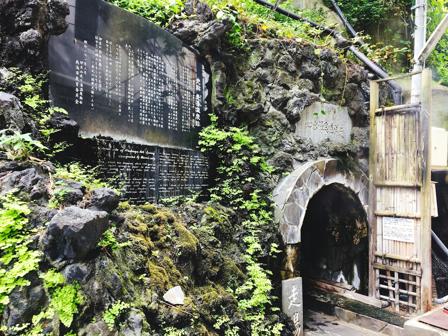 Vue pittoresque de l'entrée d'une source chaude avec un panneau entouré de rochers et de mousse