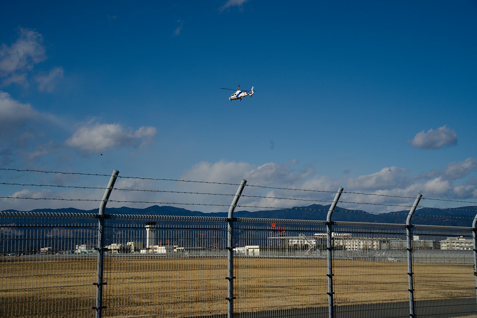 Small aircraft flying over a runway with a blue sky